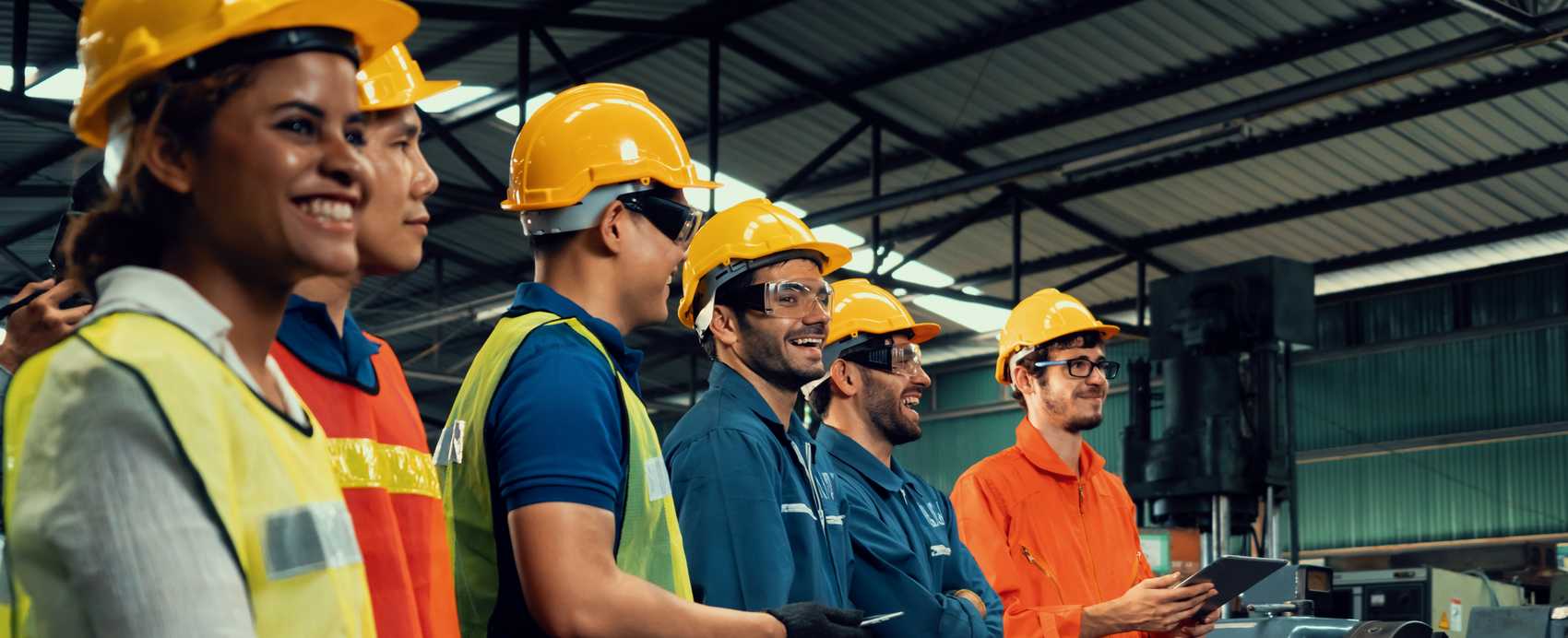 Team of industrial workers in hard hats and safety vests on a factory floor