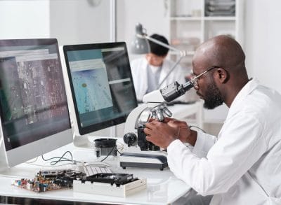 Technician examining a component under a microscope at a workbench