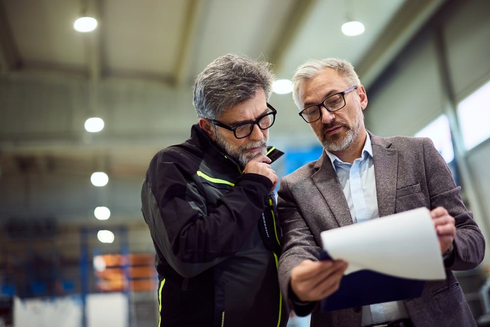 Two professionals reviewing documents inside a modern industrial facility