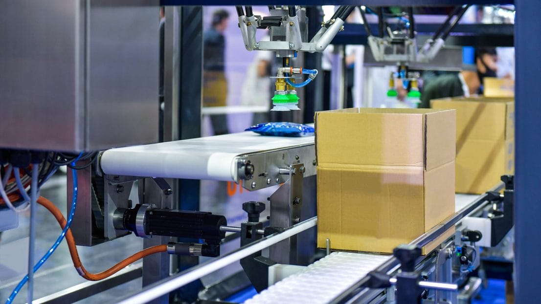 Automated packaging machine placing items into a cardboard box on a conveyor