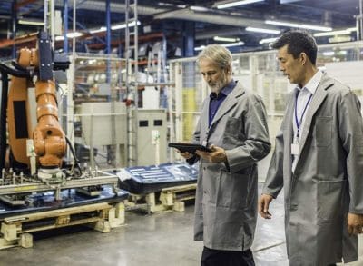 Two engineers walking a factory floor reviewing equipment on a tablet