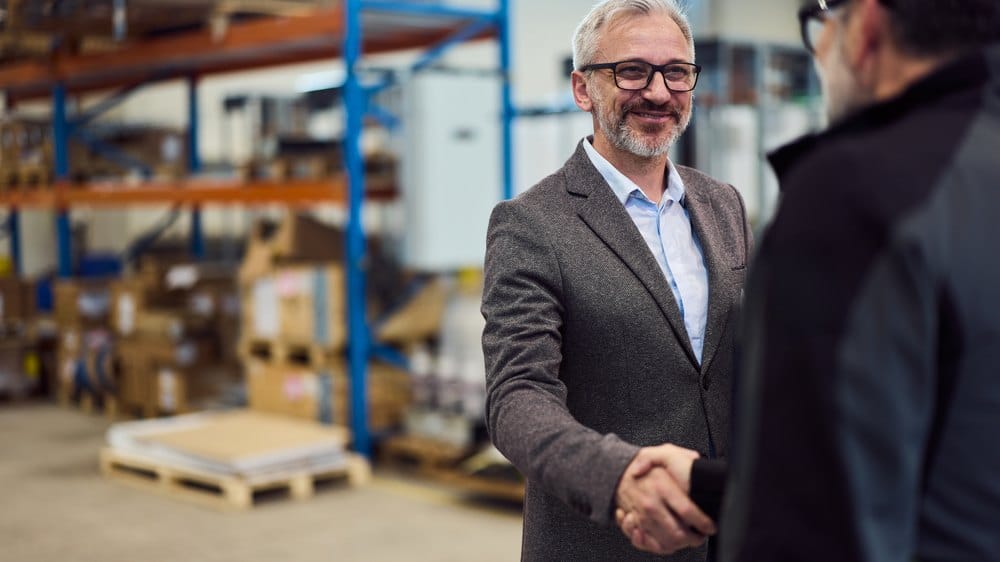 Two professionals shaking hands on a warehouse floor, backing the post-shipment guarantee