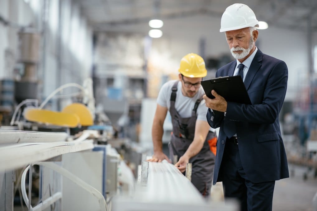 Senior engineer with a clipboard inspecting a production line with a technician