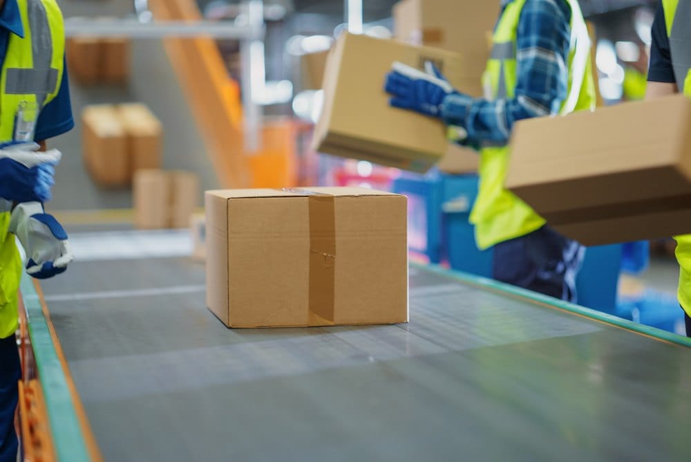 Workers placing packed boxes onto an automated conveyor for outbound shipping