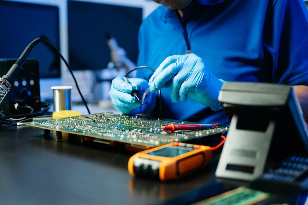 Electronics technician soldering a circuit board with precision in a repair lab